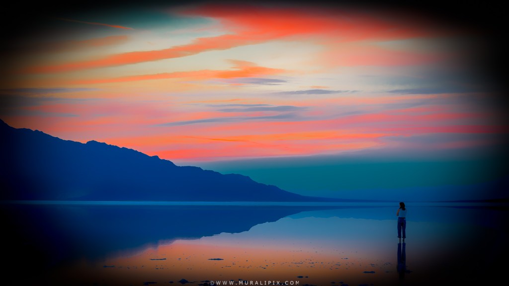A woman at a flooded Lake Manly at dusk after a storm in Death Valley National Park. Parament Mountains are in the background.